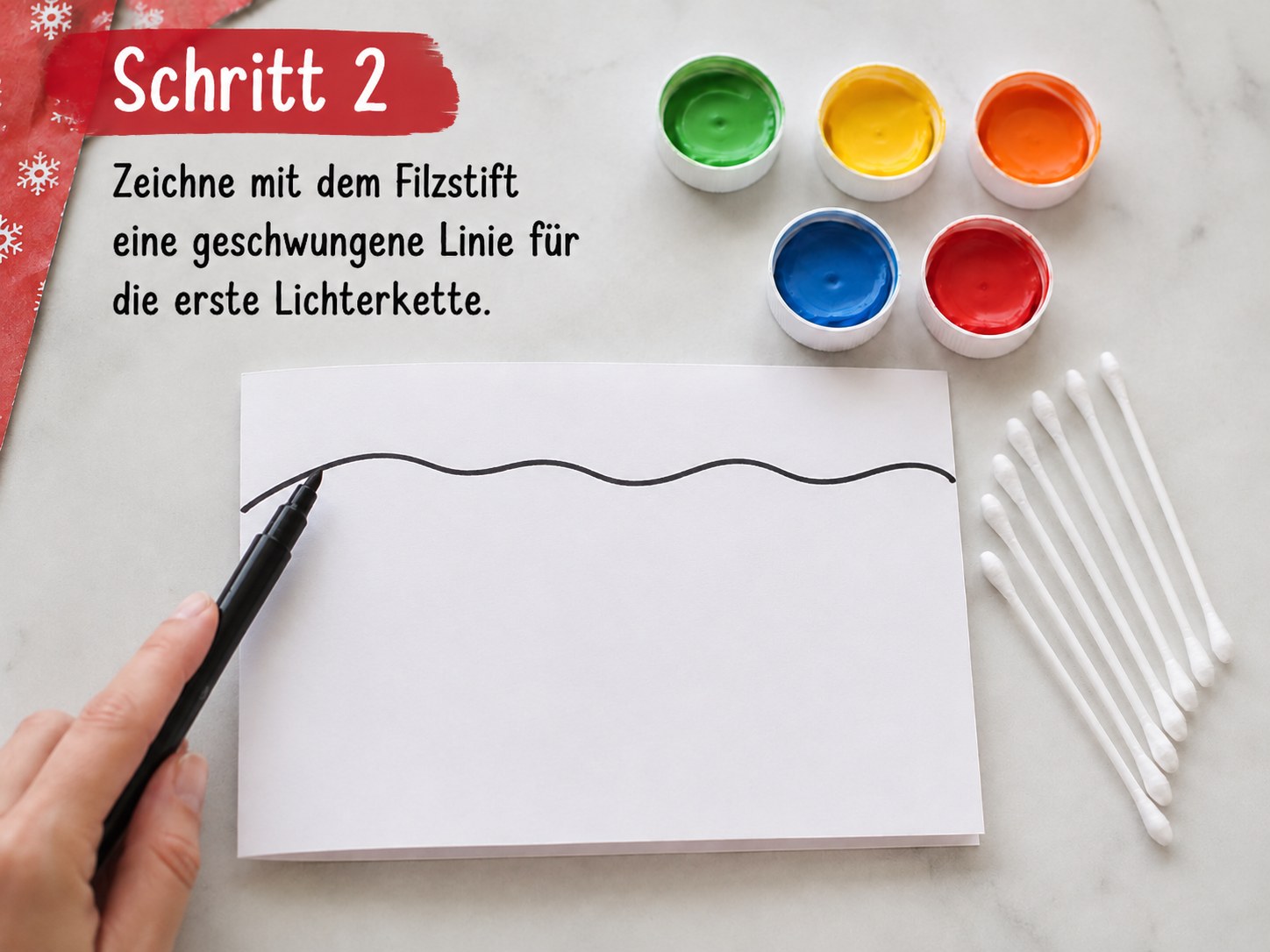 Hand zeichnet mit Filzstift eine geschwungene Linie für die erste Lichterkette auf die Weihnachtskarte
