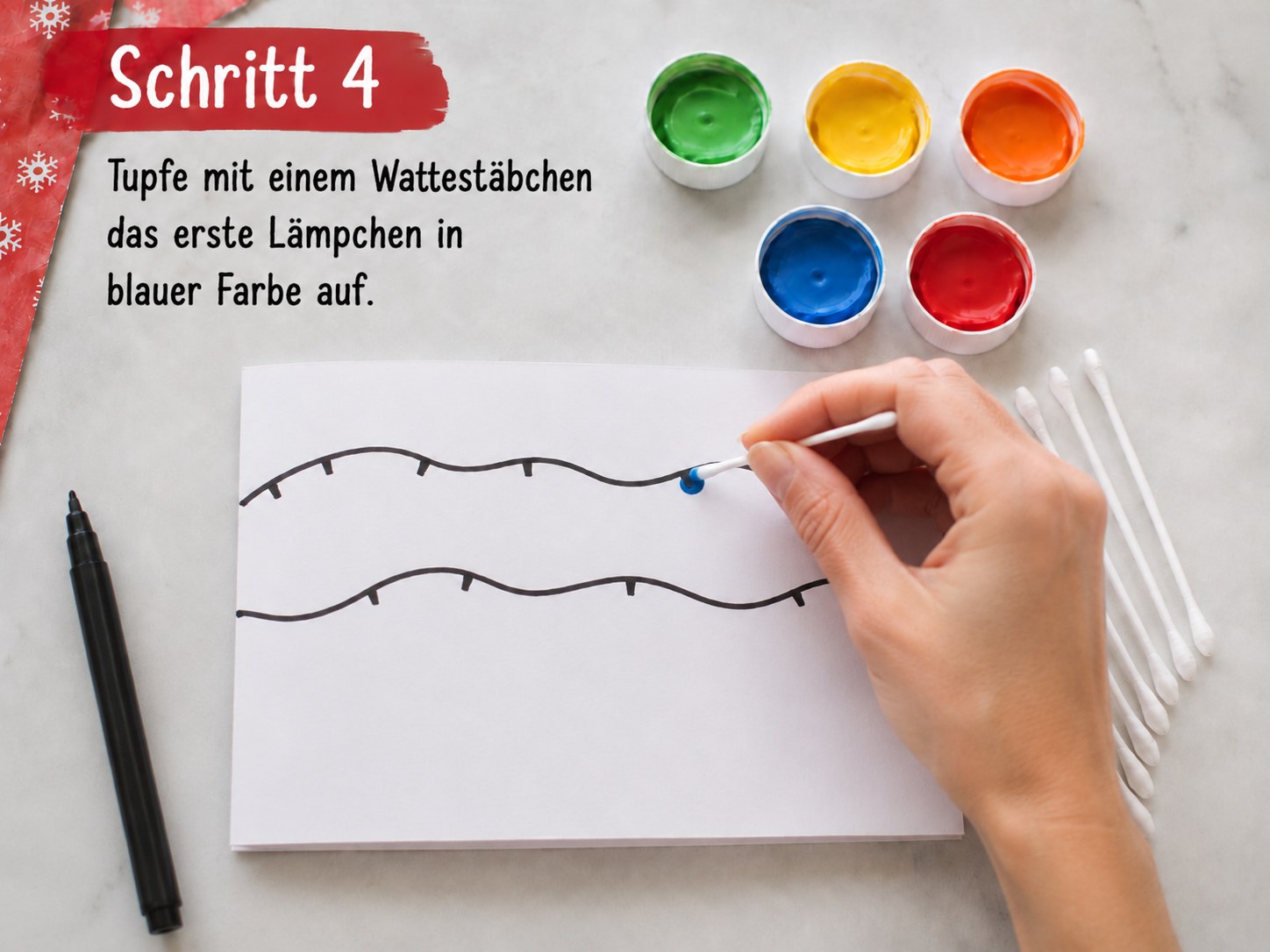 Wattestäbchen tupft das erste blaue Lämpchen auf die vorgezeichnete Lichterkette der Weihnachtskarte