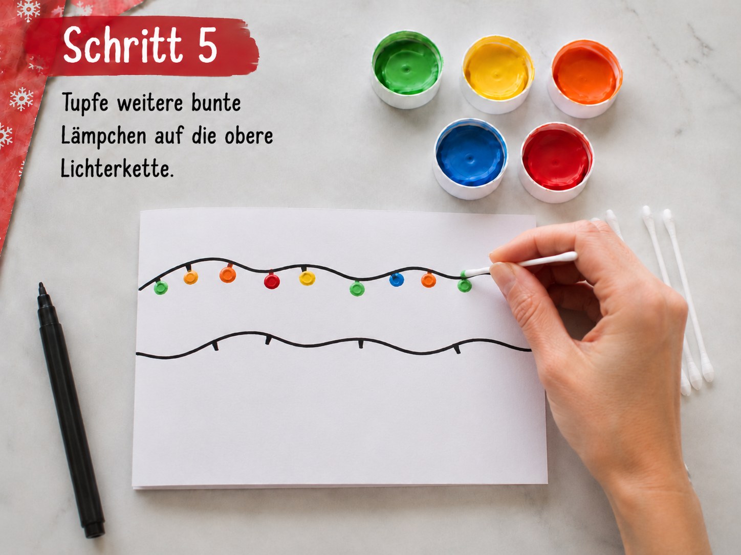 Bunte Lämpchen werden mit dem Wattestäbchen auf die obere Lichterkette der Weihnachtskarte getupft