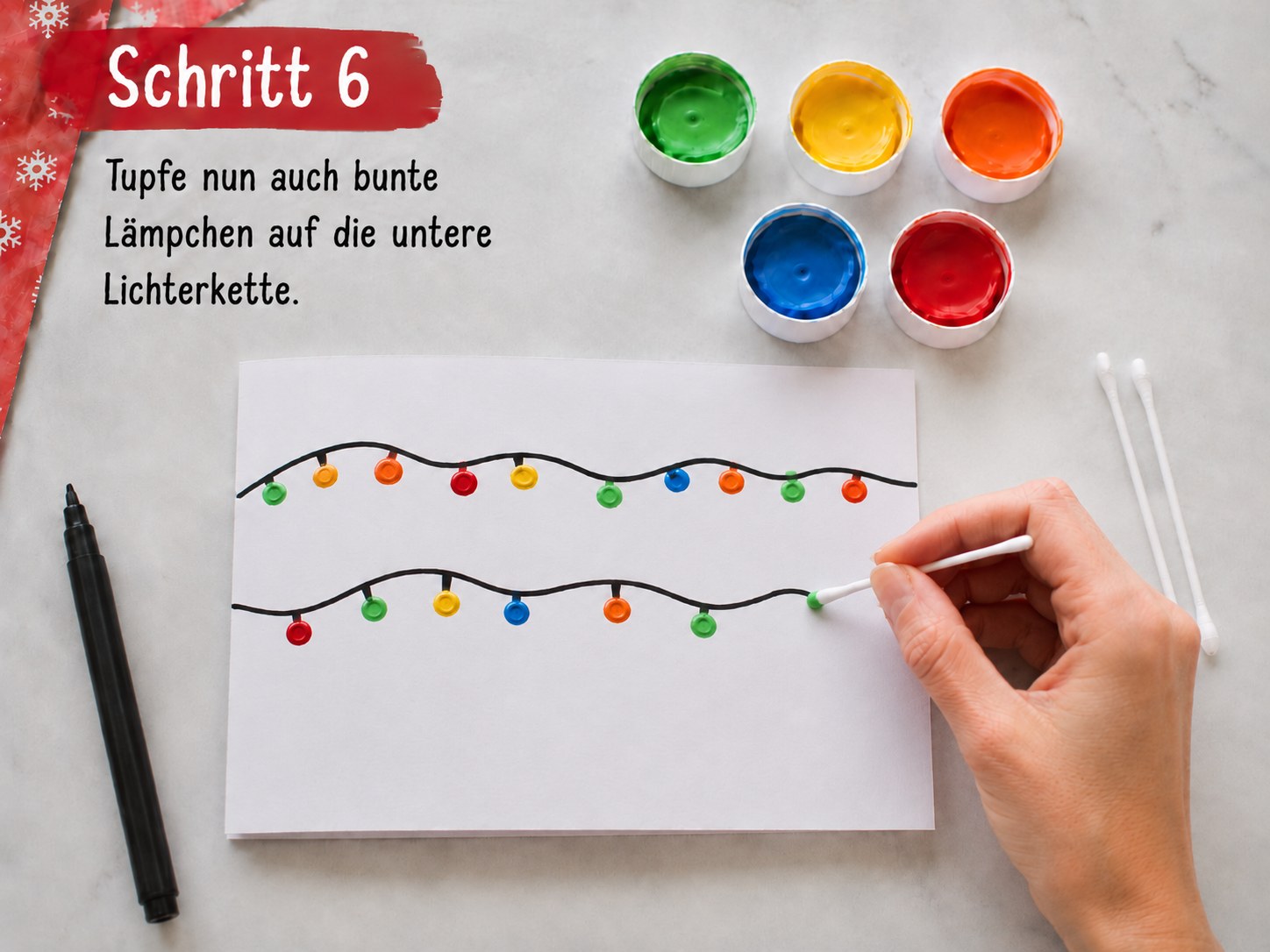 Kinderhand tupft mit Wattestäbchen bunte Lämpchen auf die untere Lichterkette der Karte