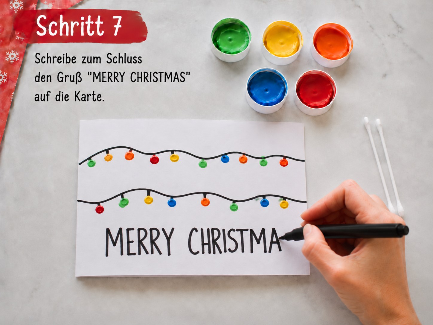 Schriftzug Merry Christmas wird mit schwarzem Filzstift unter die Lichterketten der Weihnachtskarte geschrieben
