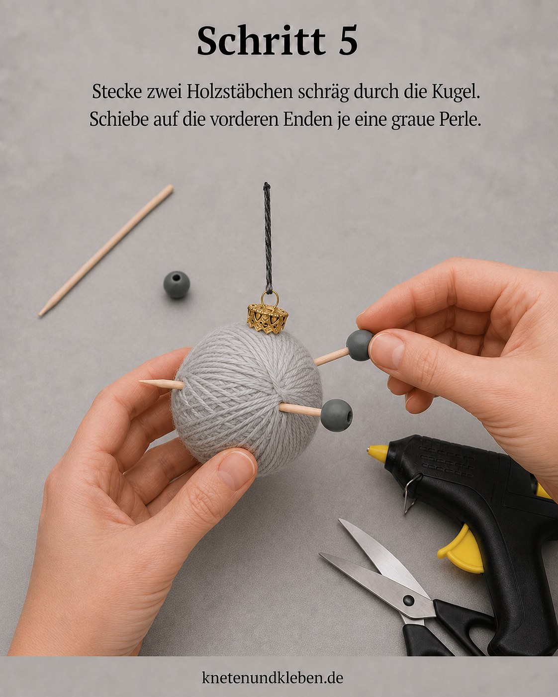 Zwei Holzstäbchen stecken schräg in der Wollkugel, graue Perlen sitzen an den Enden